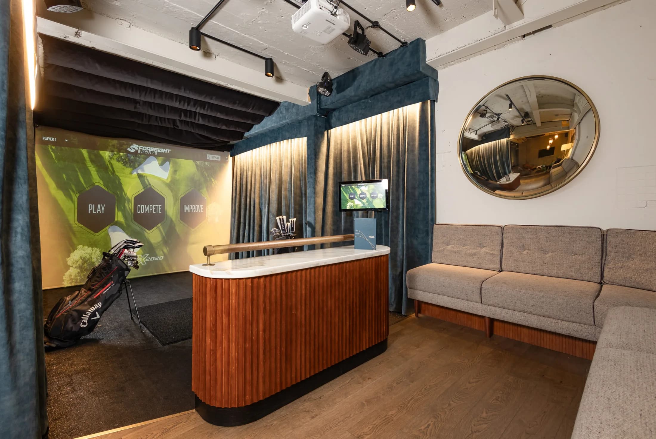 An empty Pitch simulator bay with Foresight software, seating and golf clubs.