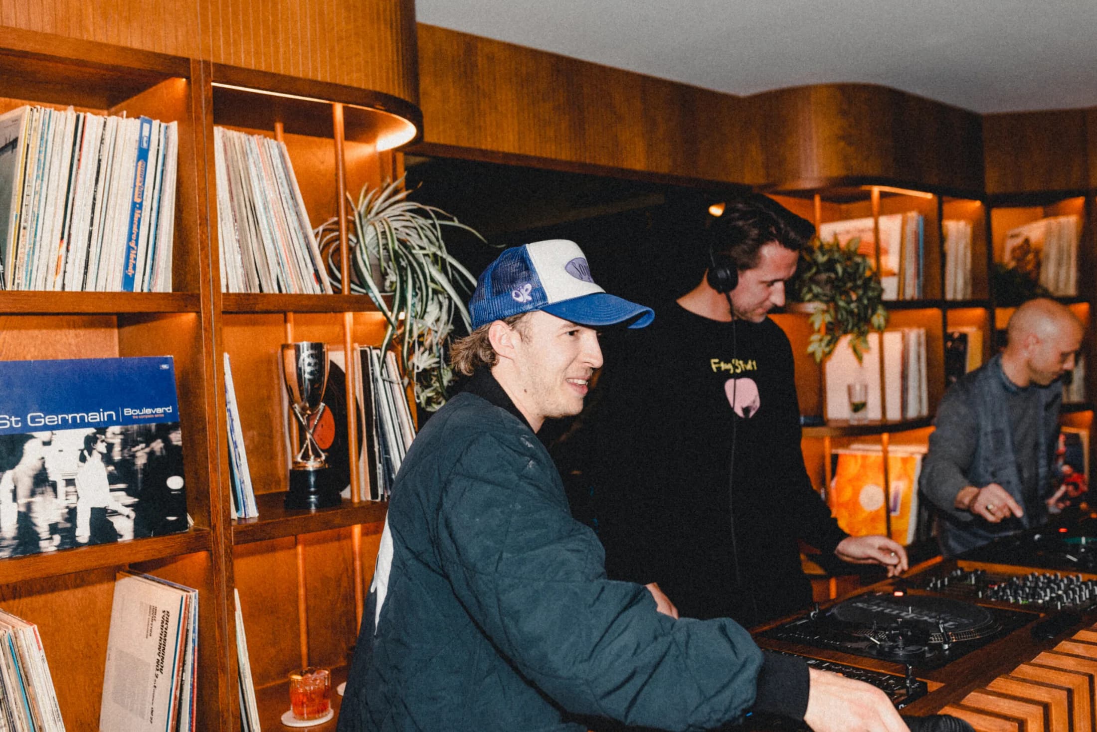 A DJ plays beside Pitch Soho's illuminated record shelves during a social event.