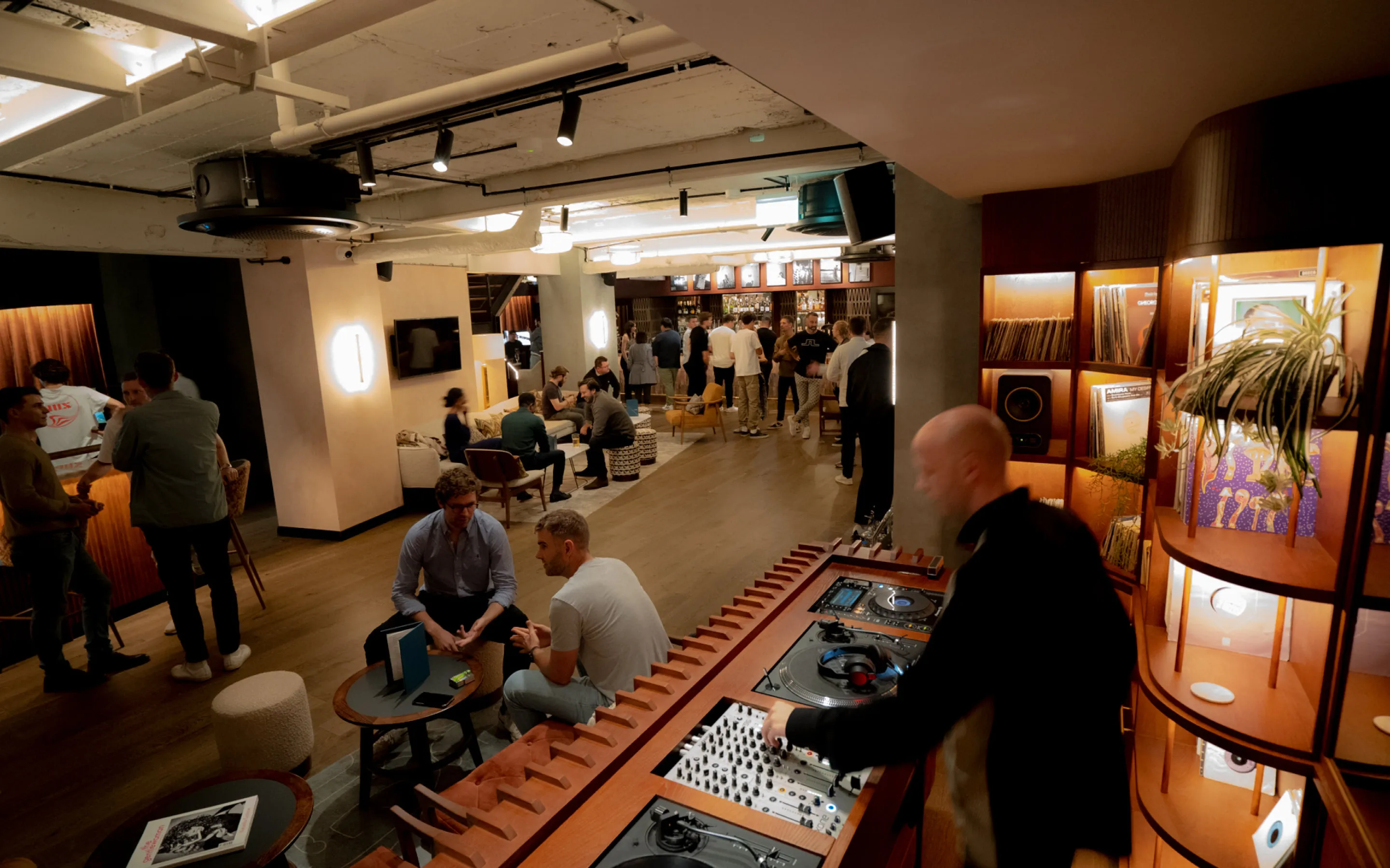 Guests socialise across the Pitch clubhouse floor while a DJ plays in the foreground.