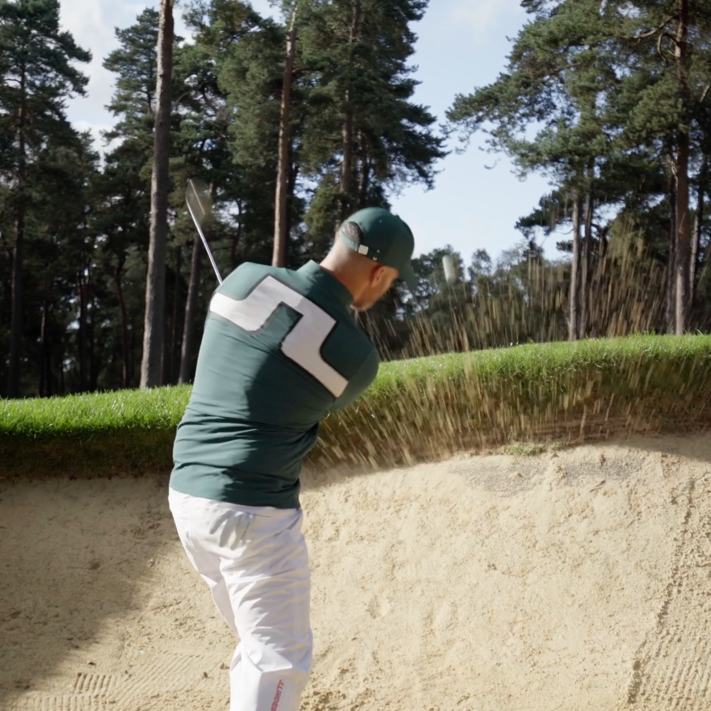 Golfer playing from a bunker in a green J.Lindeberg top at Woburn.