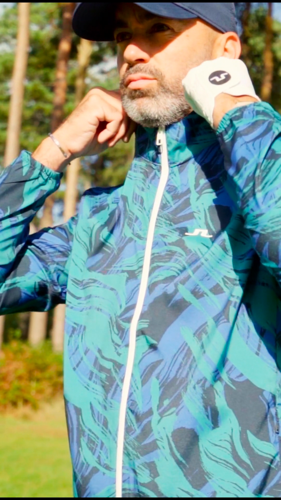 Close portrait of a golfer adjusting a blue and green patterned J.Lindeberg jacket in woodland at Woburn.