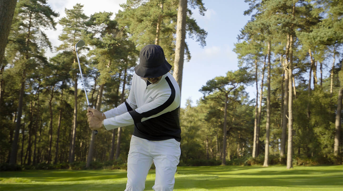 Golfer in a monochrome J.Lindeberg layer making a close-range practice swing at Woburn.