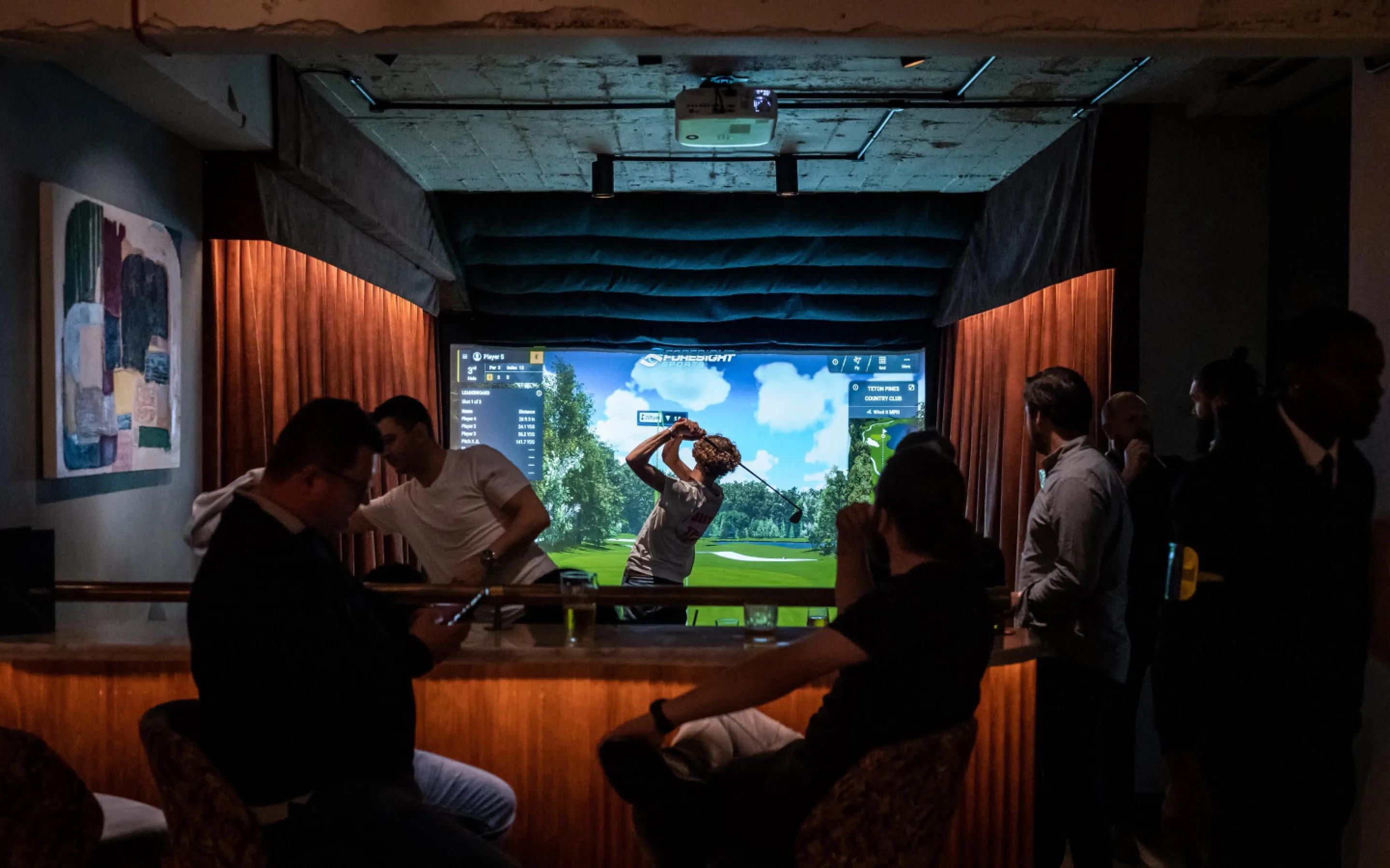 Guests gather around a golfer using an indoor simulator at Pitch Golf London.